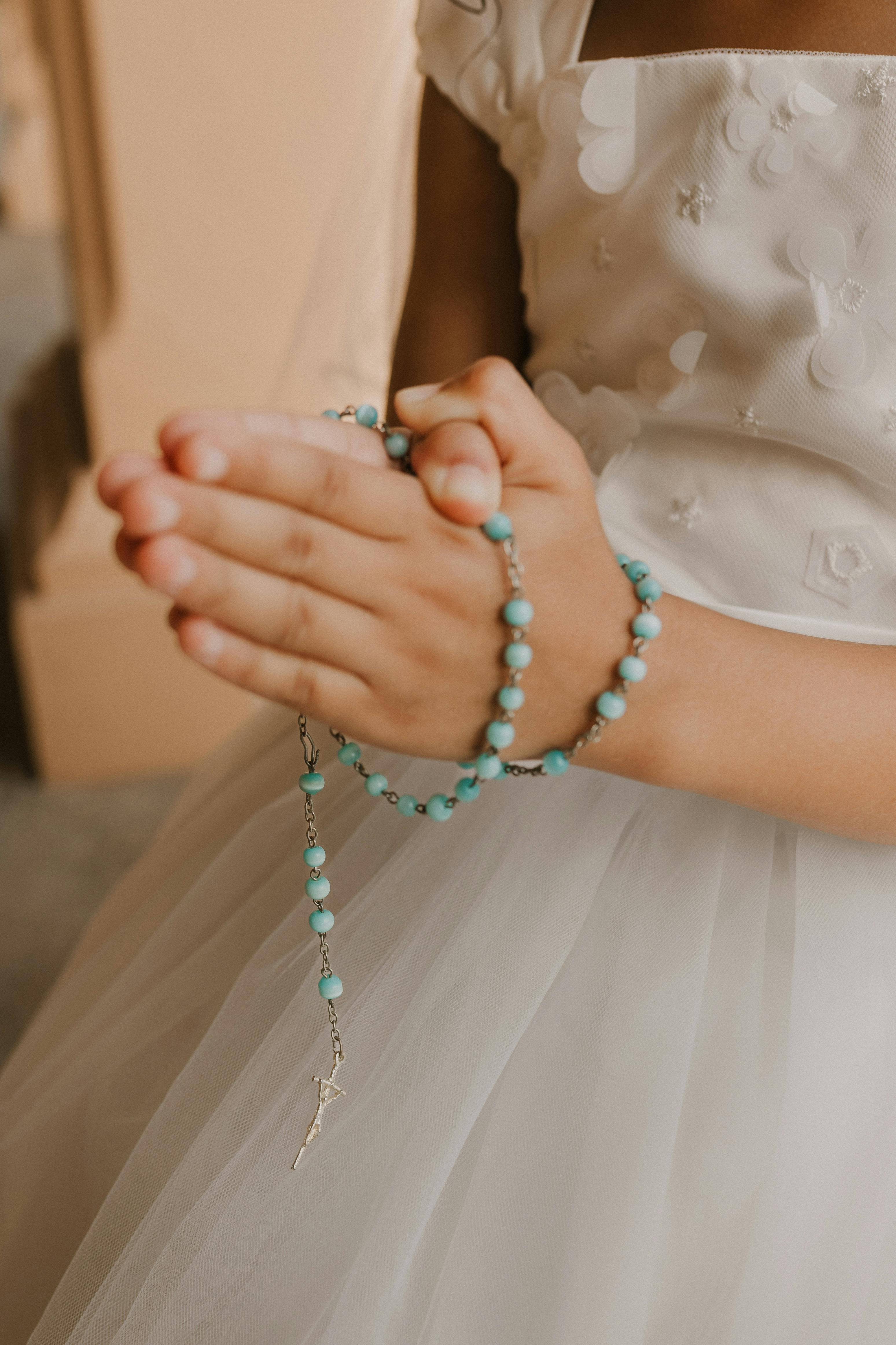 Girl's hands holding a light teal rosary beads