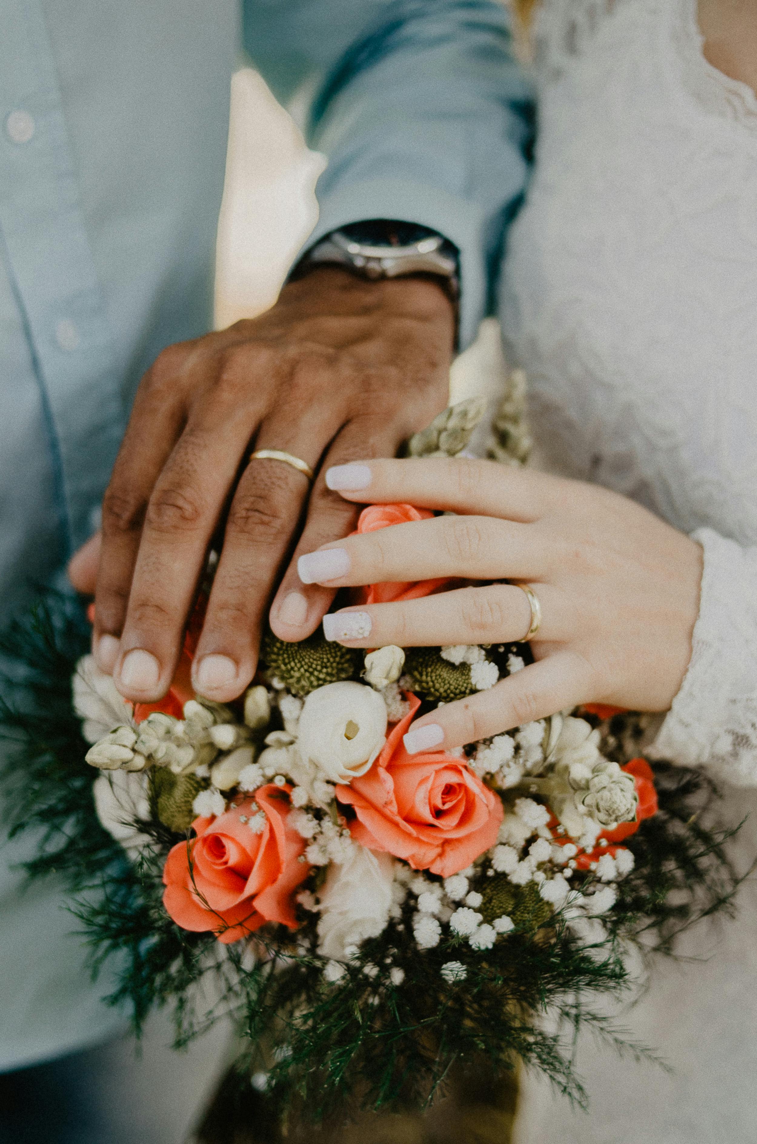 A bride and groom's hands resting on a bouquet
