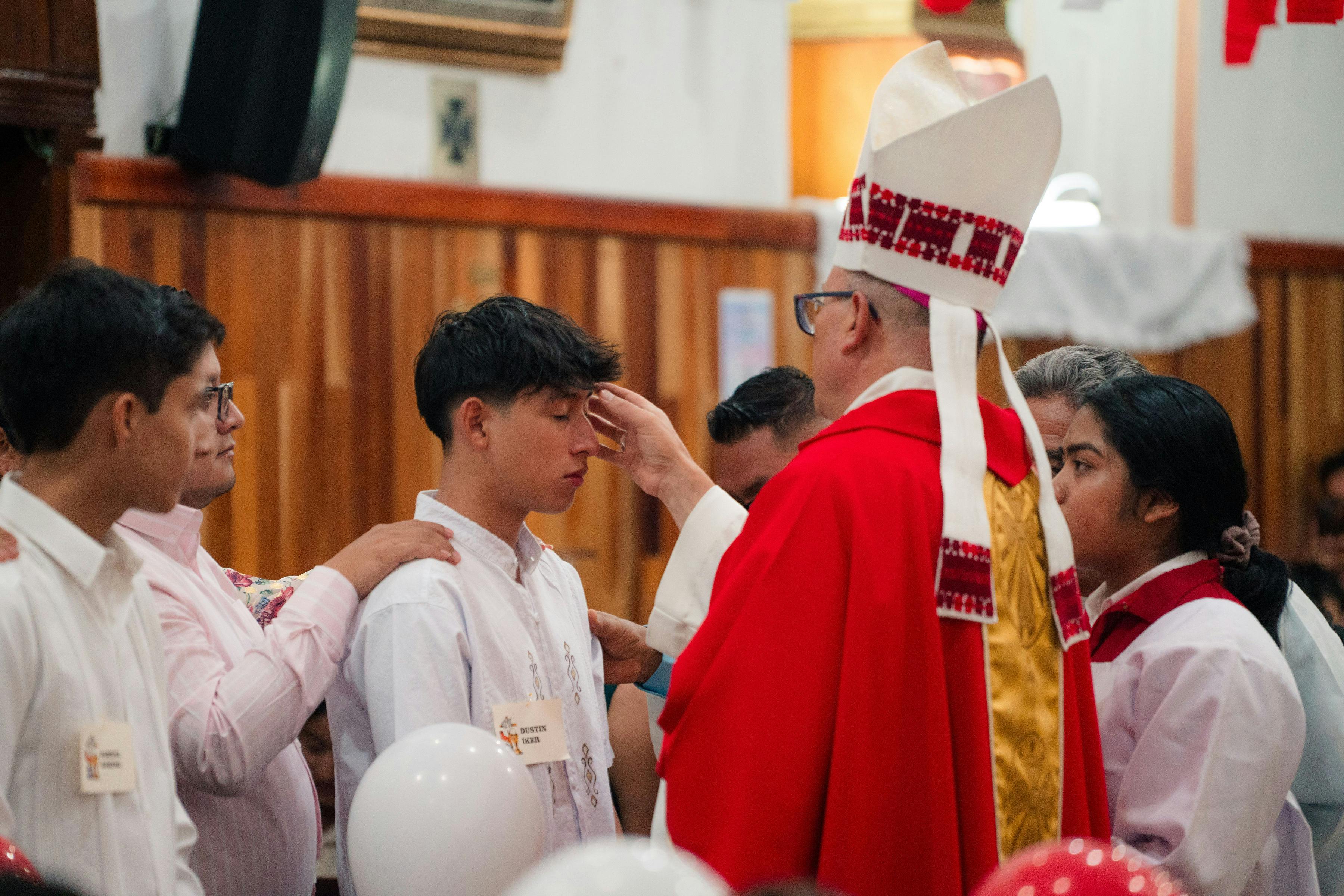 A bishop in a red robe placing his hand on a man's forehead